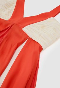 Punane ja valge varrukateta kleit, millel on volditud kreemjas ülakeha ja V-kaelusega disain, asetatud lamevalgele taustale.