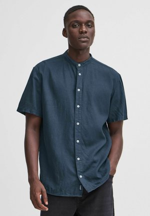Camisa de manga corta en color navy con cuello mao, cierre de botones en la parte delantera y un corte relajado. Fabricada con un tejido texturizado.