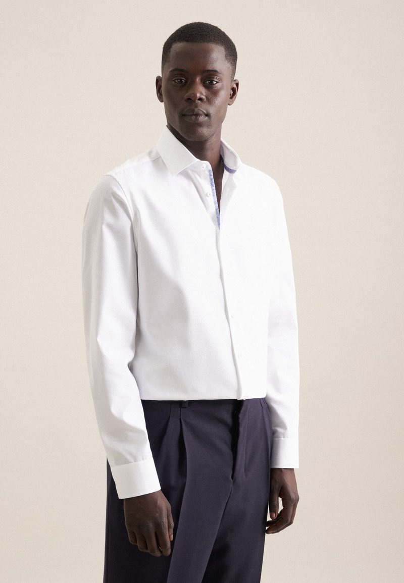 Camicia bianca con colletto a fantasia in contrasto, design aderente, maniche lunghe e tessuto morbido. Indossata con pantaloni scuri.