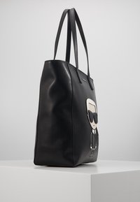 Black leather tote bag with twin handles, featuring a cartoon design on the front. Smooth texture and structured shape.