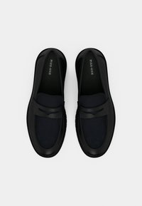 Μαύρα παπούτσια χωρίς κορδόνια με υφασμένη μπλε λεπτομέρεια και λείες μαύρες πινελιές. Διαθέτουν στρογγυλεμένο σχήμα και αντίθετη μαύρη λουρίδα.