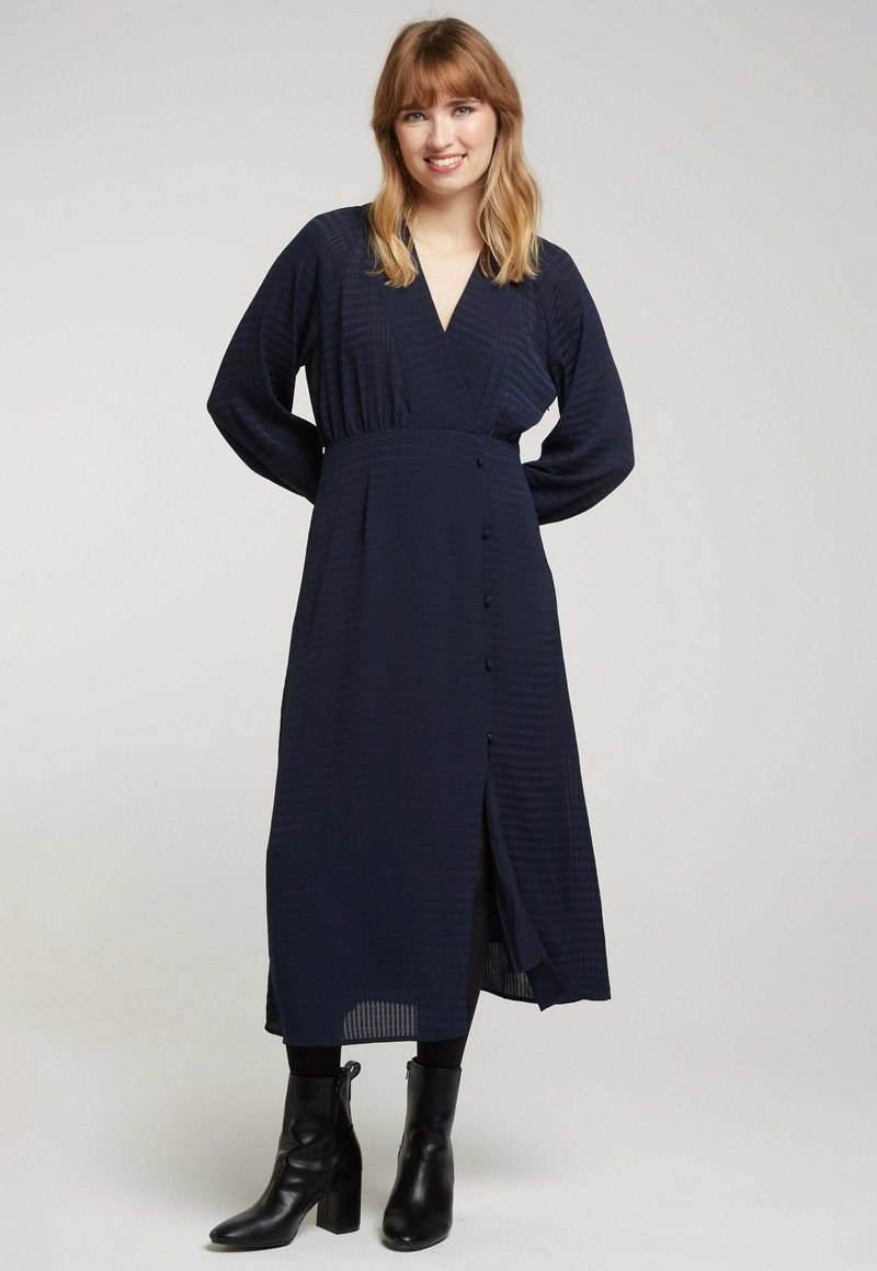 Robe cache-cœur marine à manches longues, avec un décolleté en V profond, des boutons à l'avant et une fente sur le côté ; tissu texturé avec des lignes subtiles.