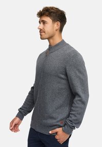Sweat à zip gris avec un col et des poignets côtelés, doté d'une tirette en bois et d'un petit logo en bas à gauche.