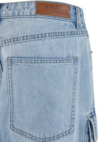 Lyseblå jeans i denim med et lædermærke mærket "URBAN CLASSICS." Har et struktureret design, synlige sømme og detaljer i baglommen.