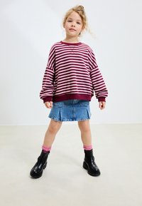 Sweter w bordowo-białe paski z luźnymi rękawami, do tego niebieska spódnica dżinsowa i czarne botki za kostkę, z różowymi, dzierganymi skarpetkami.