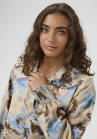 Hosszú ujjú felső, csomózott festési mintával kék, barna és krémszínben. Puha anyag, smockölt csuklódíszítéssel és laza szabással.