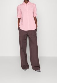 Ljusrosa kortärmad skjorta med krage, i kombination med vida grå byxor. Inkluderar strumpor med svart och vit zebramönster. Slät tygtextur.