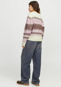 Gebreid sweater met horizontale strepen in lichtgroen, roze en bruin, voorzien van geometrische patronen; gecombineerd met losse blauwe denim jeans.