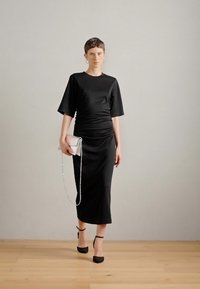 Μαύρο midi φόρεμα με κοντά μανίκια και φάρδυνση στη μέση, συνδυασμένο με μια μικρή ασημί τσάντα και μαύρα σανδάλια με λουριά.