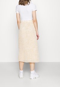 Plisserad midikjol i ett ljusbeige tyg med en mjuk textur. Stylad med en vit figursydd t-shirt och vita sneakers.