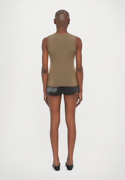 Top marrone senza maniche realizzato in tessuto a costine, abbinato a pantaloni corti neri con stampa grafica e design aderente. Scarpe nere piatte visibili.