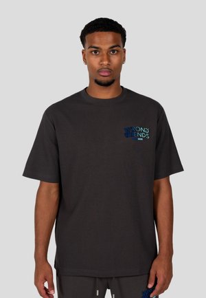 Camisa de gran tamaño gris, de mangas cortas, con el logotipo multicolor "AMIGOS INCORRECTOS" en el lado izquierdo del pecho. Tejido suave y corte relajado, con costuras mínimas.