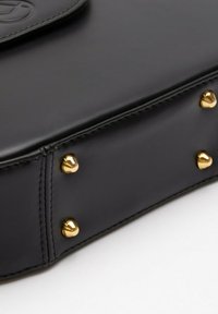Čierna kožená kabelka s hladkou textúrou, zlatými kovovými doplnkami a štyrmi zaoblenými kovovými nýtmi na spodnej strane pre zvýšenú stabilitu.