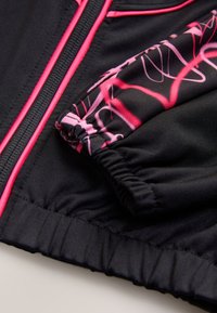 Black sports jacket with pink accents. Features a zip closure and patterned sleeve detail. Fabric has a smooth texture with elastic cuffs.