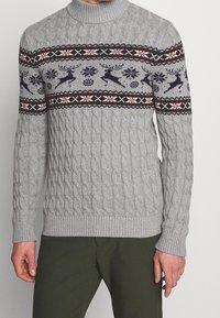 Grijze kabelgebreide trui met een geribbelde kraag en zoom, met een feestelijk fair isle patroon van rendieren en sneeuwvlokken in marineblauw, rood en wit.