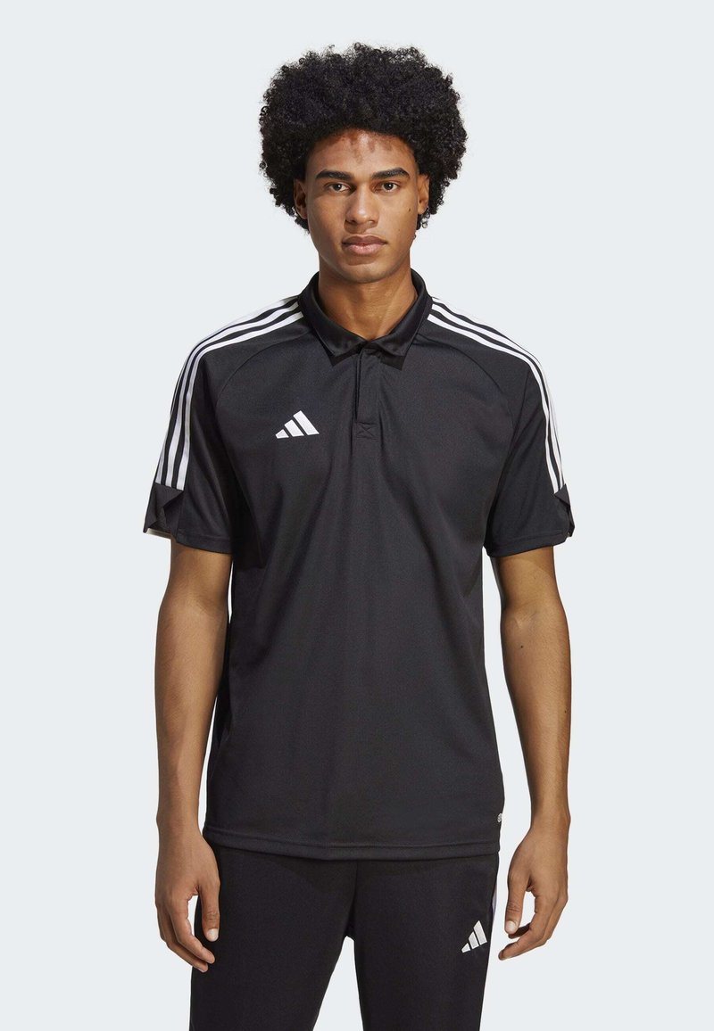 Polo shirt nero a maniche corte con colletto, caratterizzato da un design a tre strisce bianche sulle spalle e un logo Adidas sul lato sinistro del petto.