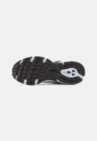 Zwart-witte zool van een sportieve schoen met een gestructureerd rubberen oppervlak, prominente loopvlaklijnen en twee blauwe accenten nabij de hiel.