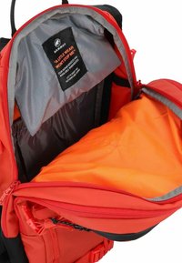 Czerwony plecak od wewnątrz z szarym wykończeniem i pomarańczową komorą. Posiada czarną etykietę, solidne zamki i praktyczne elementy designu.
