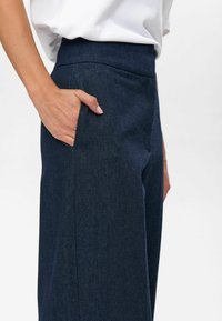 Dark blue denim pants featuring a high waistband and a side pocket, with a smooth texture and tailored fit.