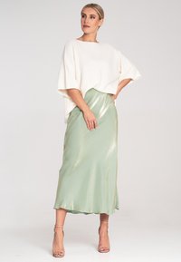 Weißes, übergroßes Oberteil mit Fledermausärmeln, kombiniert mit einem satinartigen, minzgrünen Unterrock, der ein dezentes, glänzendes Finish und eine fließende Silhouette aufweist.