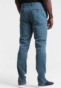 Pantaloni in misto cotone di un blu chiaro, con una texture liscia, dotati di due tasche posteriori con bottone e design a gamba dritta.