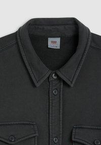 Camisa de mezclilla negra con cuello abotonado, dos bolsillos en el pecho y botones oscuros. La tela tiene un acabado texturizado. Etiqueta de Levi's en el cuello.
