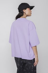 Lilac oversized t-shirt with short sleeves, made of soft cotton. Paired with black patterned pants and a black cap. Simple design.