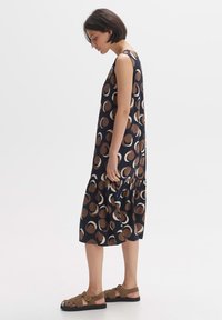 Navy dress with large brown and cream circular patterns, sleeveless design, gathered hem, paired with brown sandals. Smooth fabric texture.
