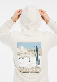 Felpa color crema con un grafiche di montagne innevate, sci e una seggiovia sul retro. Tessuto morbido con una vestibilità comoda.