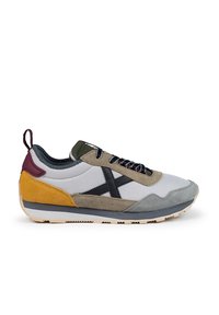 Zapatilla con una mezcla de malla gris, acentos de ante en amarillo, marrón y oliva, con un diseño de logo negro, suela texturizada y cordones redondos.