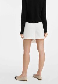 Czarny sweter z długim rękawem i falbaniastym wykończeniem, zestawiony z białymi szortami i jasnobeżowymi balerinkami z czarnym czubkiem.