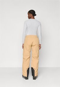 Calças cargo bege com um corte relaxado, apresentando bolsos laterais e detalhes em preto nas bainhas. Usadas com uma blusa de manga longa cinza-claro.