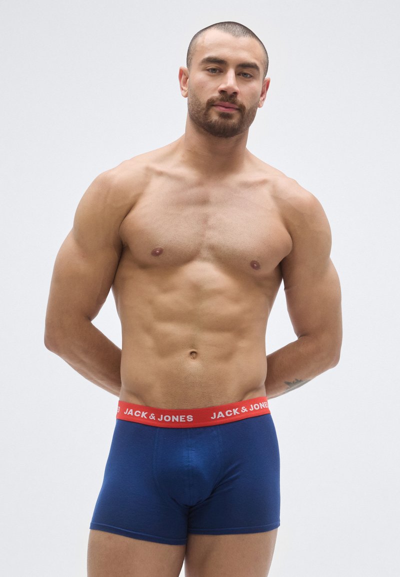 Cuecas boxer em algodão azul-marinho, com cintura elástica vermelha estampada com o texto "JACK & JONES". Textura lisa, design ajustado.