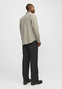 Chemise à manches longues à carreaux beige et marron foncé, avec un col classique et des poignets à boutons, assortie à un pantalon noir ajusté et des chaussures noires.