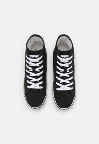 Czarne trampki typu high-top wykonane z płótna, z białymi sznurowadłami, z białą metką z logo, gumową podeszwą i kontrastowym wykończeniem wzdłuż krawędzi.