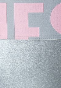 Γκρίζο ύφασμα με μεγάλες ροζ γράμματα στην επάνω περιοχή. Η κάτω περιοχή είναι από γυαλιστερό ασημί υλικό με ομαλή υφή και αντανακλαστική επιφάνεια.