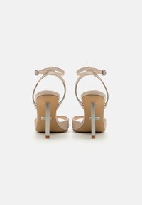 Korkokenkät, joissa on beige väri, teksturoitu hihna, avonainen takapää ja kapea metallinen korko. Varustettu säädettävällä nilkkahihnalla ja pehmeällä pohjalla.