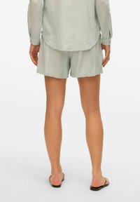 Lichtgroene shorts van een linnenmix met een relaxte pasvorm, met een zachte textuur en een elastische tailleband, gecombineerd met eenvoudige sandalen.