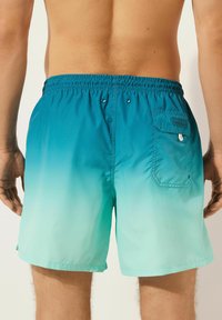 Herrbadbyxor i en gradient från teal till aqua, med resårmidja, sidofickor och en bakficka med knappstängning.