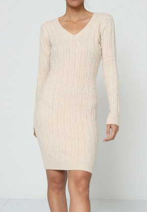 Robe en tricot beige avec décolleté en V, manches longues et coupe ajustée, arborant un motif à cable texturé et des poignets côtelés.