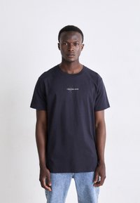 Navy blue cotton t-shirt with short sleeves and a round neckline, featuring a small white "Calvin Klein Jeans" logo on the chest.