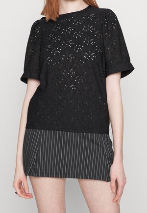 Czarna koronkowa bluzka z krótkimi bufkami, zdobiona skomplikowanymi wzorami z wycięciami. Połączona z czarną spódnicą w prążki. Minimalistyczny design.