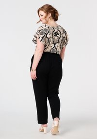 Kortarmige top met een crème- en zwart bloemenpatroon, gecombineerd met zwarte tapse broek en lichtgekleurde blokhakken.