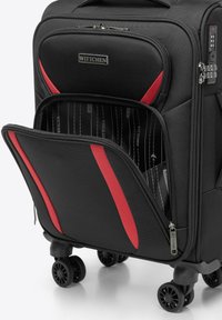 Černý kufr na kolečkách s červenými akcenty, se strukturálním povrchem, dvojitými zipy a přední kapsou, která odhaluje vzorované vnitřní prostory.