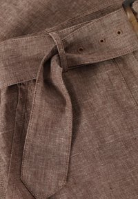 Ruskea pellavakankainen vyö, joka on pujotettu lenkkien läpi, ja jossa on näkyvä kilpikonnakuorivastus sekä ommellut napinreiät texturetulla materiaalilla.