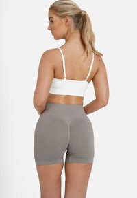 Visoko pasu, svetlo sivi športni šortlji z gladko teksturo. Pairs z oprijeto belo kratko majico z nastavljivimi trakovi.