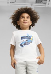 Camiseta blanca de manga corta con un gráfico azul y negro de un coche de carreras con llamas y el texto "PUMA". Combinada con pantalones de chándal grises.