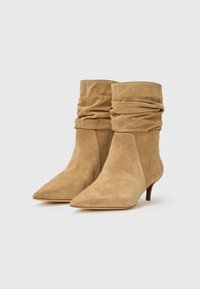 Stivaletti alla caviglia in suede beige con un design sformato, punta affusolata e tacco basso. Texture liscia con un aspetto morbido e informale.