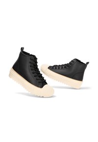Zapatillas altas negras con suelas gruesas acanaladas beiges y punteras, cordones negros y tiradores sobre fondo blanco.