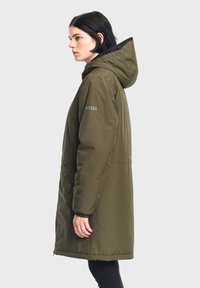 Parka rembourrée vert olive avec capuche, dotée de poignets élastiques, d'une fermeture éclair à l'avant et d'un détail de logo sur la manche. Texture lisse.